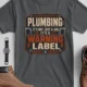 Plumbing Warning Label T-Shirt — Funny Plumber Shirt — asphalt t-shirt, flat-lay product photo | Pressure Tested Co