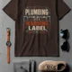 Plumbing Warning Label T-Shirt — Funny Plumber Shirt — brown t-shirt, flat-lay product photo | Pressure Tested Co