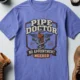 Plumber T-Shirt — "Pipe Doctor. No Appointment Needed" Vintage Work Shirt — flo-blue — Flat-lay Plumber T-Shirt — "Pipe Doctor. No Appointment Needed" Vintage Work Shirt — flo-blue t-shirt, flat-lay product photo | Pressure Tested Co