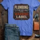 Plumbing Warning Label T-Shirt — Funny Plumber Shirt — heather-columbia-blue t-shirt, flat-lay product photo | Pressure Tested Co