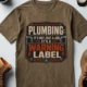 Plumbing Warning Label T-Shirt — Funny Plumber Shirt — heather-olive t-shirt, flat-lay product photo | Pressure Tested Co