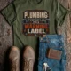 Plumbing Warning Label T-Shirt — Funny Plumber Shirt — military-green t-shirt, flat-lay product photo | Pressure Tested Co