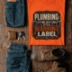 Plumbing Warning Label T-Shirt — Funny Plumber Shirt — orange t-shirt, flat-lay product photo | Pressure Tested Co