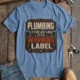 Plumbing Warning Label T-Shirt — Funny Plumber Shirt — steel-blue t-shirt, flat-lay product photo | Pressure Tested Co
