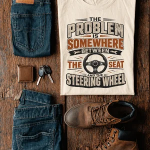 Driving Humor T-Shirt — "The Problem Is Somewhere Between The Seat And The Steering Wheel" — natural t-shirt, flat-lay product photo | Pressure Tested Co