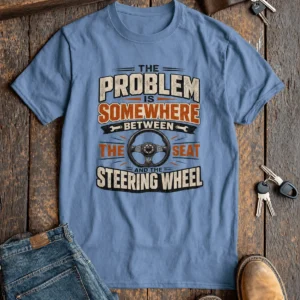 Driving Humor T-Shirt — "The Problem Is Somewhere Between The Seat And The Steering Wheel" — steel-blue t-shirt, flat-lay product photo | Pressure Tested Co